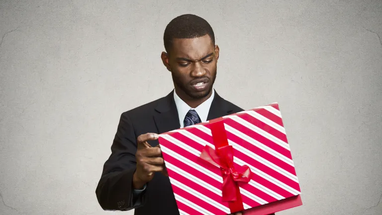A man holding a wrapped gift looking at it.